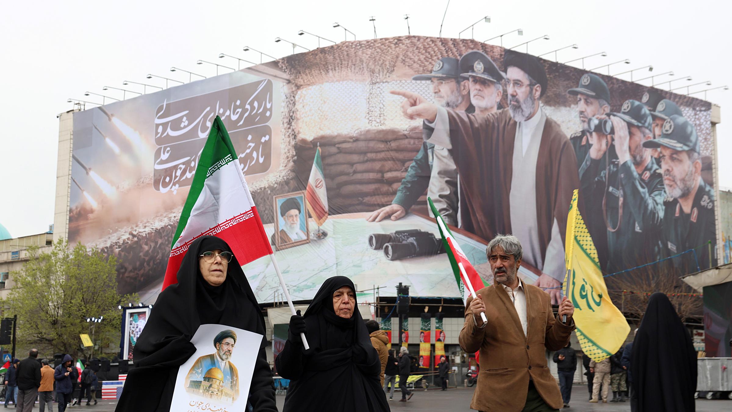 Iraner gehen während einer Kundgebung zum Internationalen Al-Quds-Tag am 13.03.2026 in Teheran, Iran, vor einer Plakatwand vorbei, auf der der oberste Führer des Iran, Modschtaba Chamenei, und iranische Militärkommandanten zu sehen sind. 