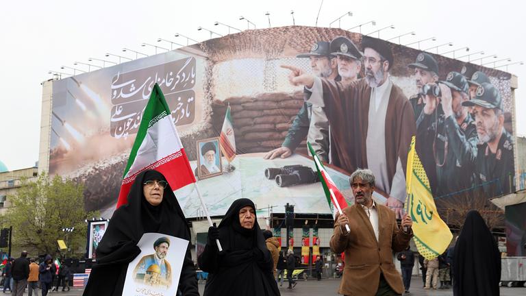 Iraner gehen während einer Kundgebung zum Internationalen Al-Quds-Tag am 13.03.2026 in Teheran, Iran, vor einer Plakatwand vorbei, auf der der oberste Führer des Iran, Modschtaba Chamenei, und iranische Militärkommandanten zu sehen sind. 