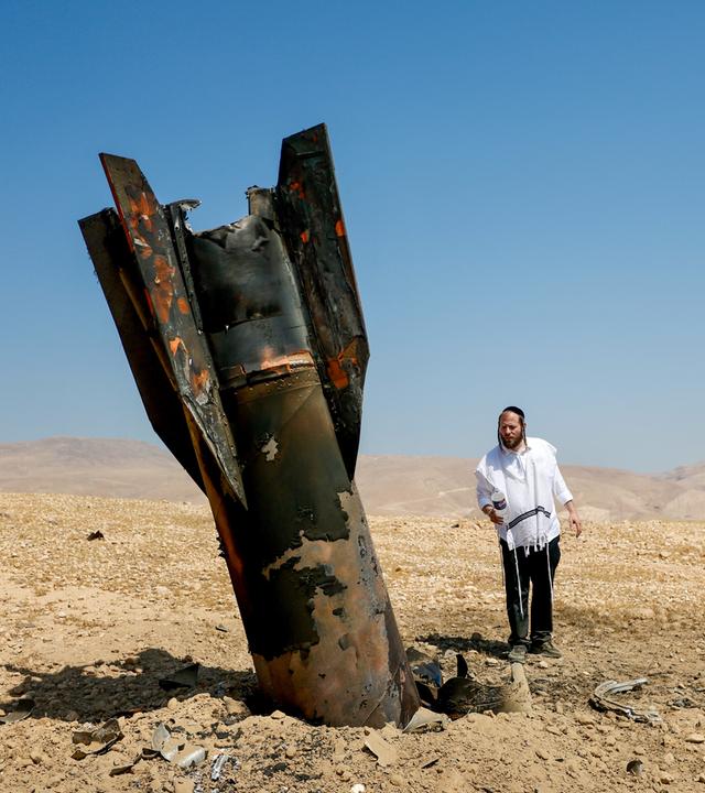 Zwei Männer inspizieren das Wrack einer Rakete, die nach einem iranischen Angriff nahe der Stadt Jericho im Westjordanland aus dem Boden ragt. 