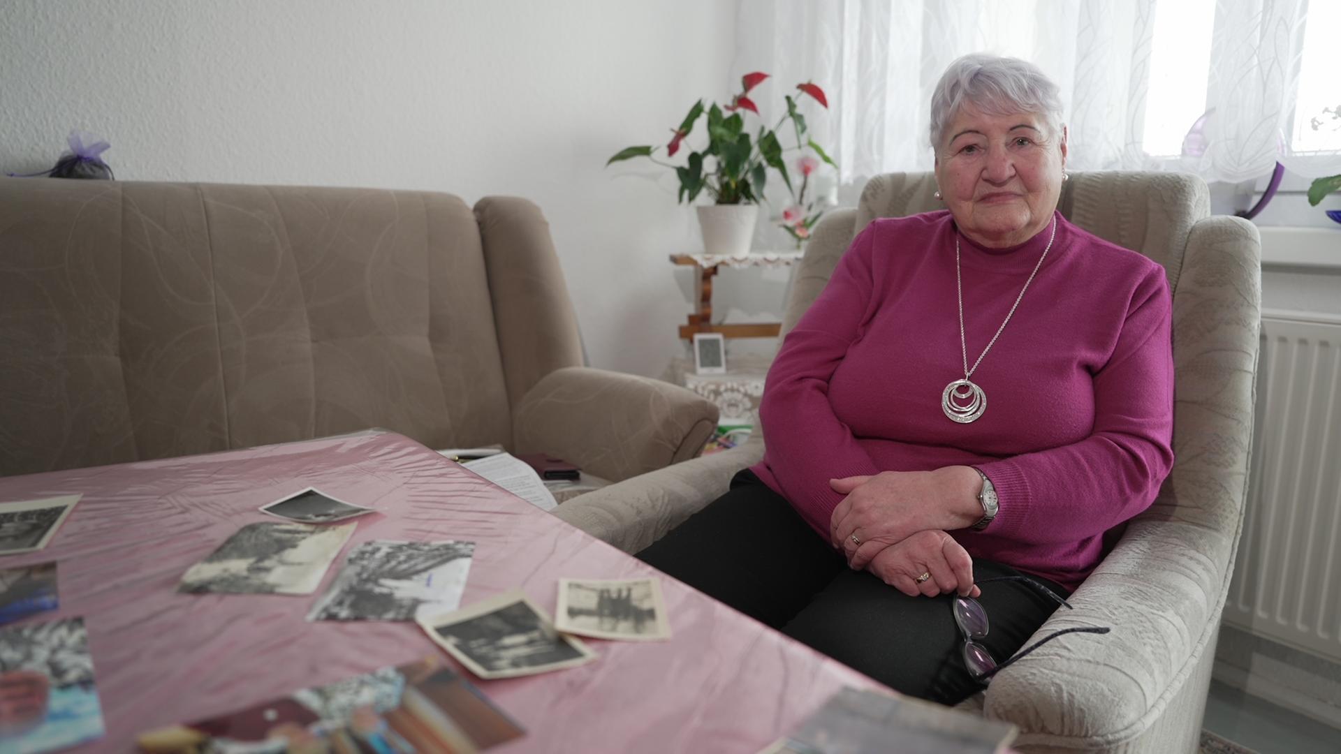 Irene Bäger auf einem Sessel sitzend mit alten Fotos vor sich auf dem Tisch liegen.