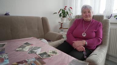 Irene Bäger auf einem Sessel sitzend mit alten Fotos vor sich auf dem Tisch liegen.