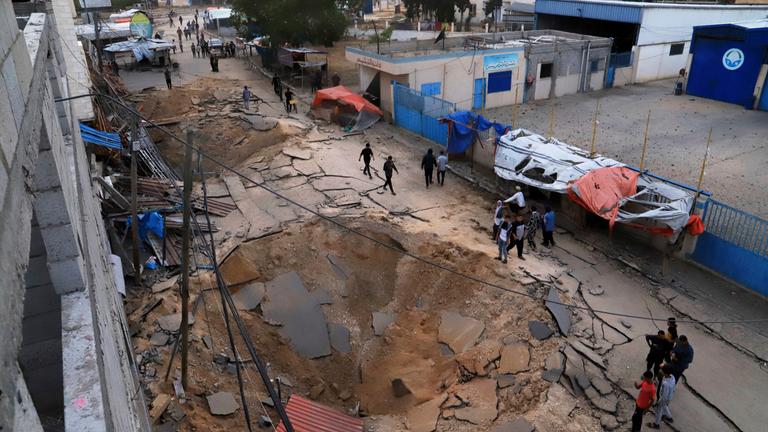  Palästinenser inspizieren den Ort eines Luftangriffs der israelischen Armee, der ein Krankenhaus in Chan Junis getroffen hat. Zu sehen ist ein Krater in einer Straße.