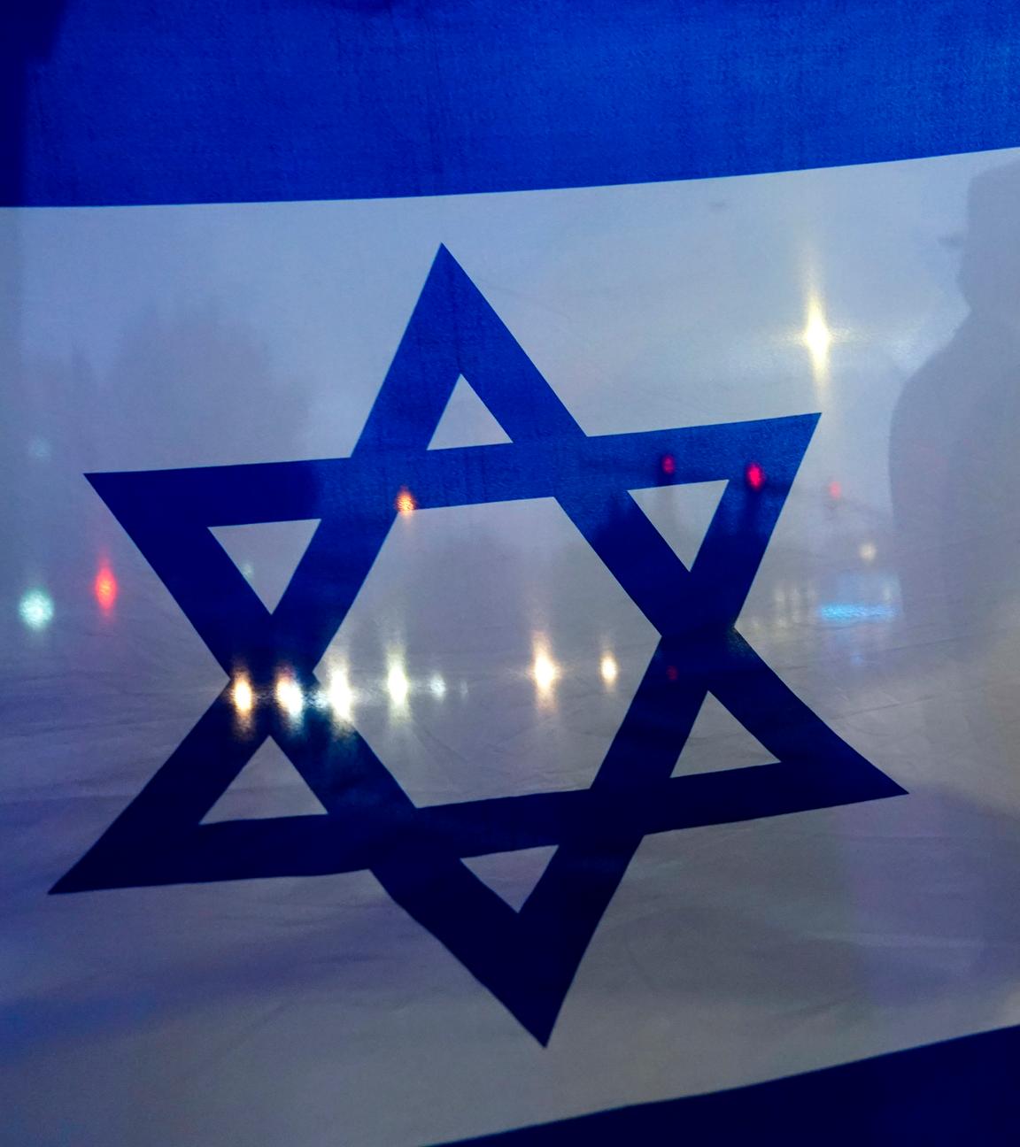 Im Vordergrund eine israelische Flagge und im Hintergrund der Straßenverkehr.