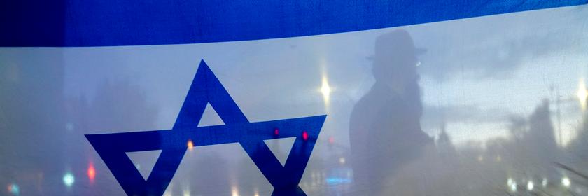 Im Vordergrund eine israelische Flagge und im Hintergrund der Straßenverkehr.