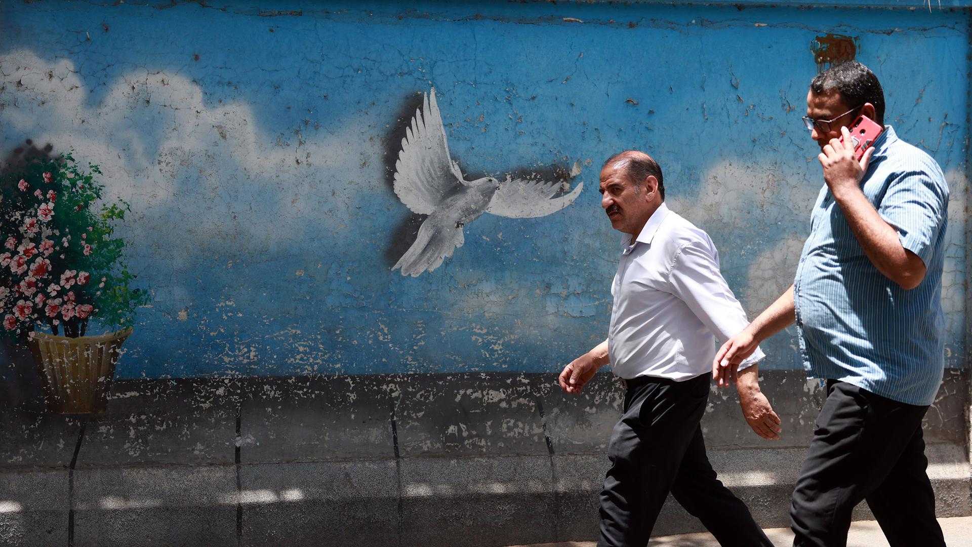Iranische Männer gehen am 24. Juni 2025 in Teheran, Iran, an einem Taubengemälde vorbei.
