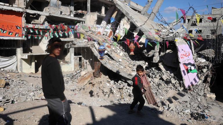 Palästinensische Jugendliche gehen durch ein vom Krieg zerstörtes Viertel.