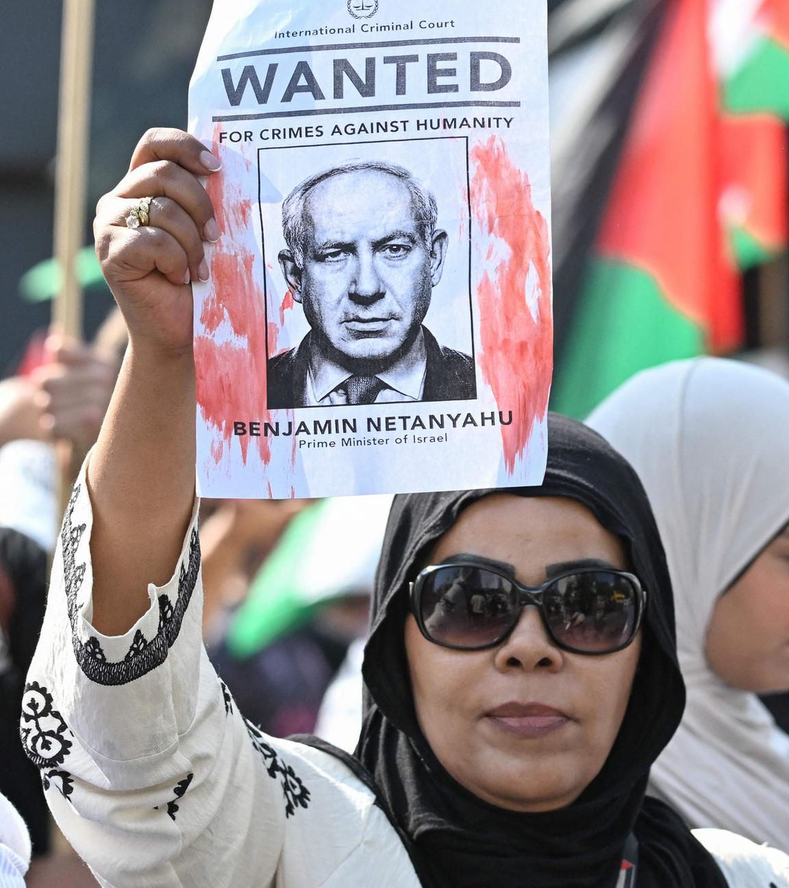 Eine Frau hält ein Wanted-Plakat von Benjamin Netanyahu hoch