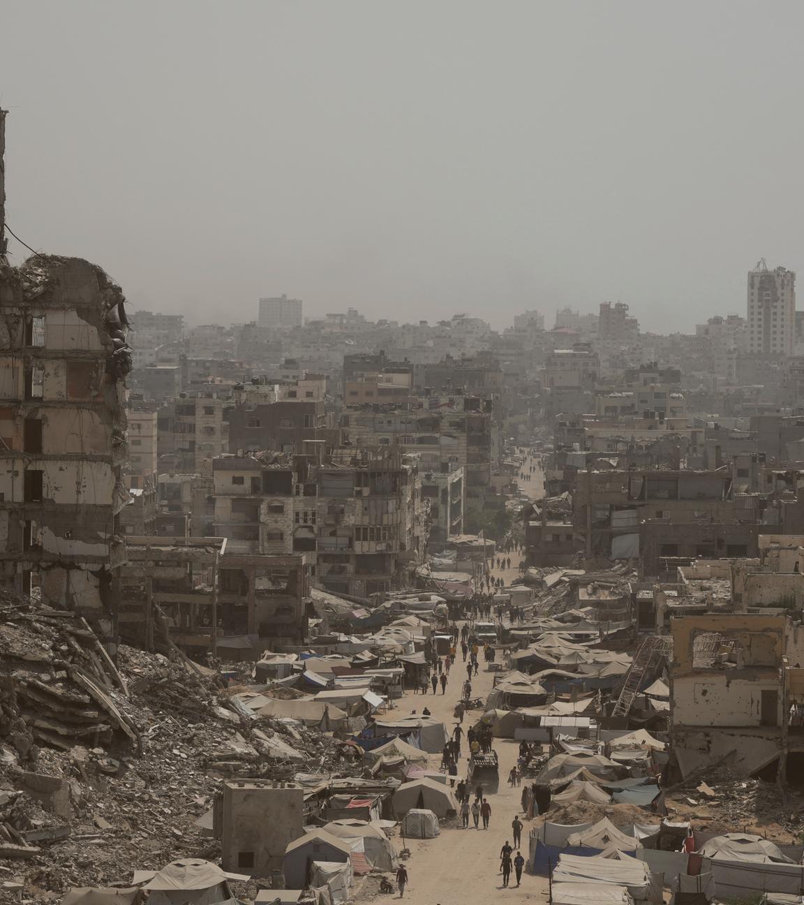 Menschen gehen eine Straße entlang, die von zerstörten Gebäuden gesäumt ist, die auf israelische Bombardierungen während des Israel-Hamas-Krieges im Gazastreifen zurückzuführen sind.