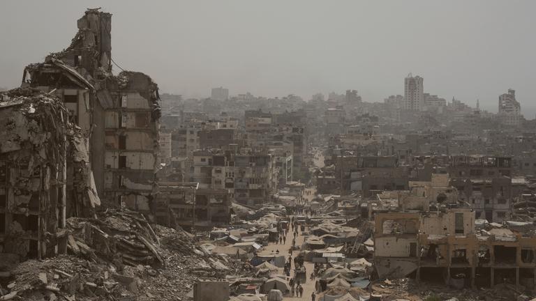 Menschen gehen eine Straße entlang, die von zerstörten Gebäuden gesäumt ist, die auf israelische Bombardierungen während des Israel-Hamas-Krieges im Gazastreifen zurückzuführen sind.