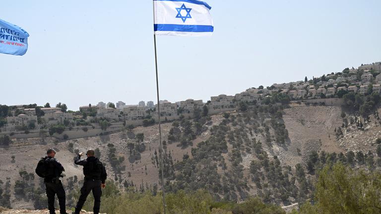 Zwei israelische Sicherheitskräfte stehen vor einer israelischen Flagge bei einer Siedlung im Westjordanland.