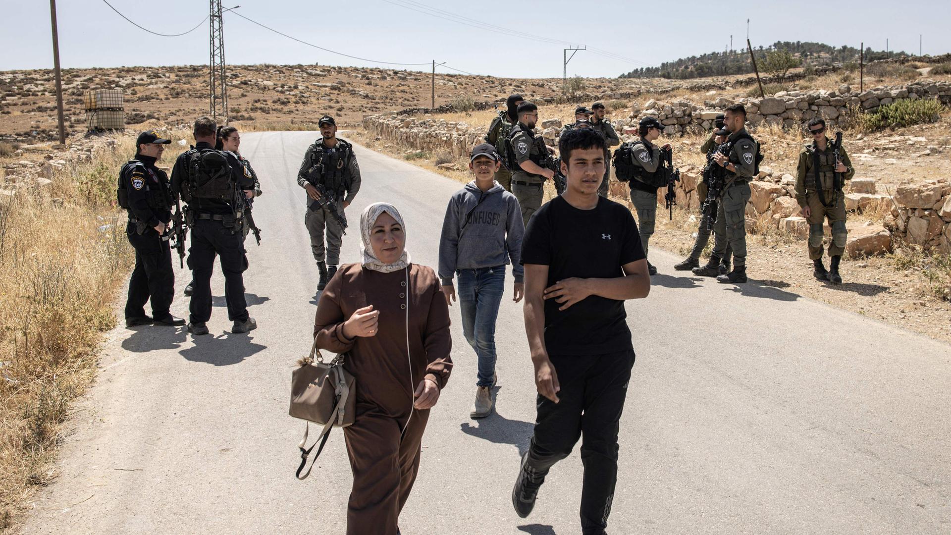 People walk past Israeli security forces as they block the entrance to the village of al-Tuwani in the Masafer Yatta area in Occupied West Bank on June 2, 2025.