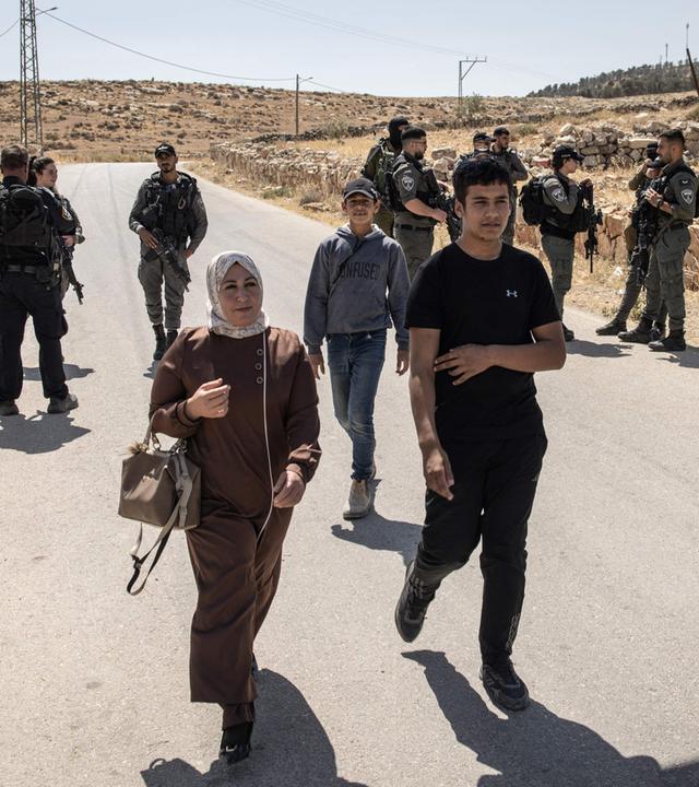 People walk past Israeli security forces as they block the entrance to the village of al-Tuwani in the Masafer Yatta area in Occupied West Bank on June 2, 2025.
