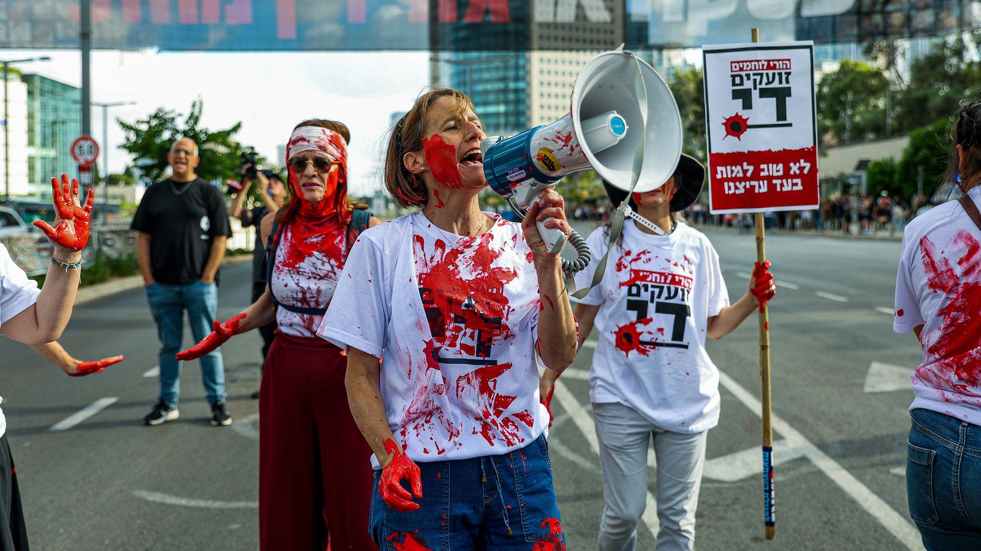 Mütter israelischer Soldaten, die im Gazastreifen kämpfen, protestieren (Mai 2024).  Sie haben rote Farbe am Körper, die Blut darstellen soll.