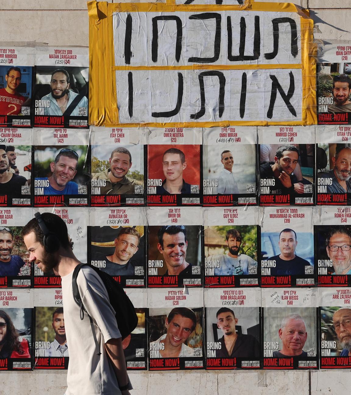 Eine Person läuft an den Bildern der Israelischen Geiseln vorbei die noch immer von der Hamas in Gaza gefangen gehalten werden. (Archiv)