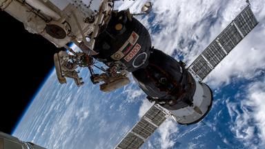 Auf dem bild sihet man zwei Kosmonauten, die ein Leck an der ISS überprüfen. Im Hintergrund sieht man einen Teil der Erde.
