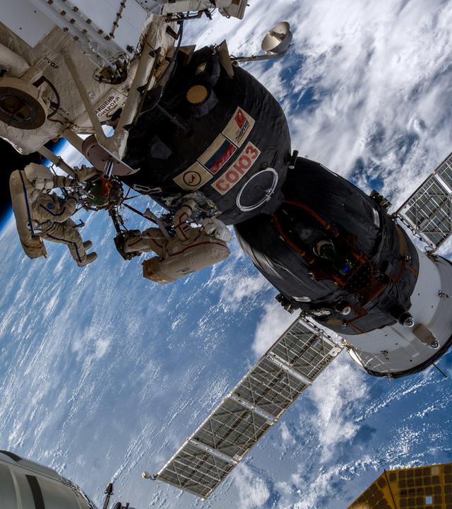 Auf dem bild sihet man zwei Kosmonauten, die ein Leck an der ISS überprüfen. Im Hintergrund sieht man einen Teil der Erde.