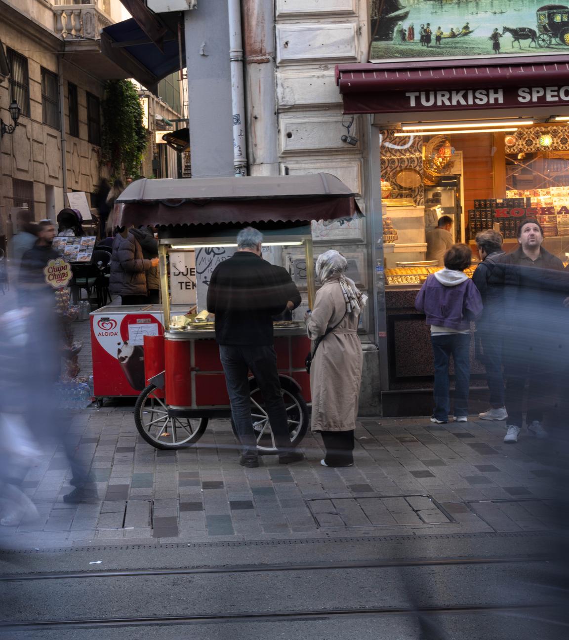  Istanbul: Menschen gehen an einem Imbissstand auf der Istiklal-Straße vorbei, einer belebten Fußgängerzone, die für ihr Street Food und ihren historischen Charme bekannt ist, 