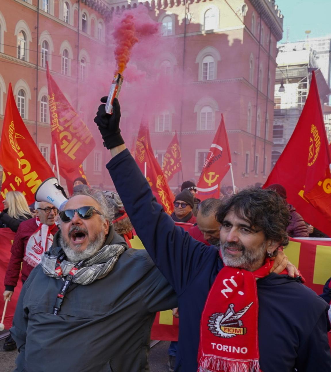 Demonstranten mit Rauchfahnen und Bannern sind in Turin auf einer Straße unterwegs. Zwei Männer sind im Vordergrund zu sehen.