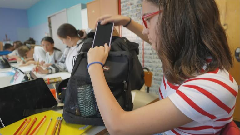 Schülerin, die ihr Handy für den Unterricht in den Rucksack steckt