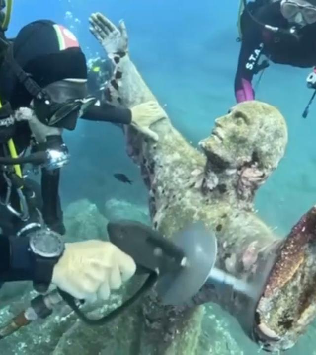 Taucher putzen die Unterwasser-Jesusstatue aus Bronze in Italien.