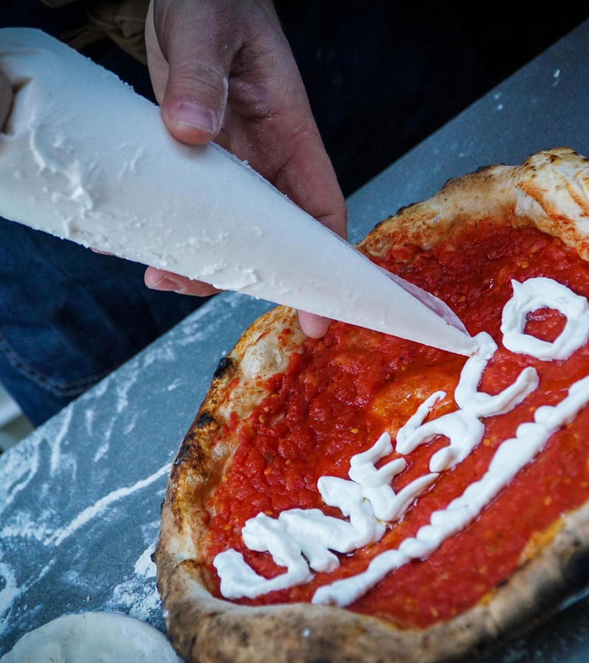 Ein Pizzabäcker schreibt den Schriftzug "Unesco" auf eine Pizza. 