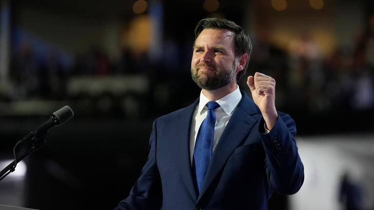 J.D. Vance steht im Anzug hinter einem Rednerpult und hebt eine geballte Faust in die Luft. 