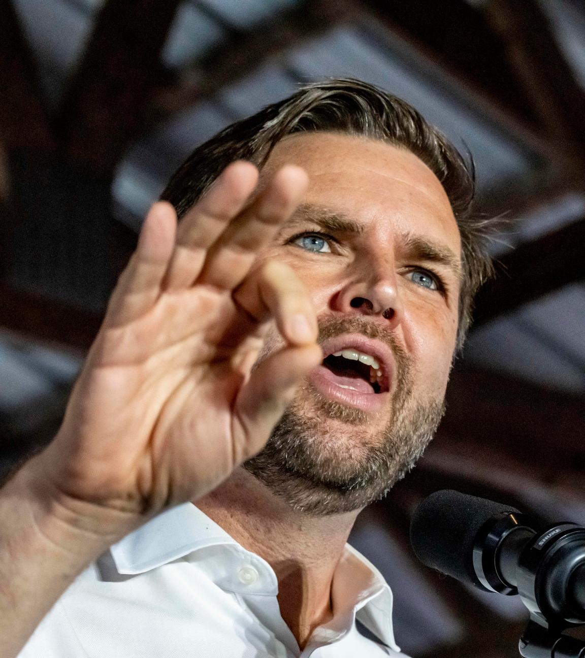 Porträtaufnahme aus Untersicht: J.D. Vance spricht in ein Mikrofon und gestikuliert mit der rechten Hand.