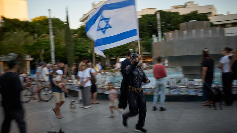 Ein als «Batman» verkleideter Mann schwenkt eine israelische Fahne, während Menschen Fotos von Israelis betrachten, die beim Terrorangriff der Hamas getötet wurden. Am 7. Oktober 2023 griffen Kämpfer der radikalislamischen Hamas Israel an, töteten zahlreiche Menschen und verschleppten Geiseln in den Gazastreifen.