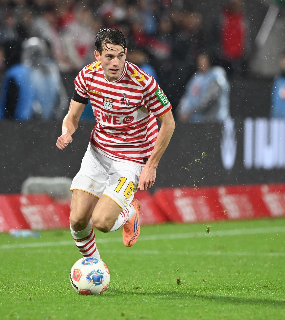 Kölns Spieler Jakub Kaminski läuft beim Spiel gegen den Hamburger SV im rot-weiß gestreiften Karnevalstrikot des 1. FC Köln mit dem Ball vor dem rechten Fuß über den Rasen.