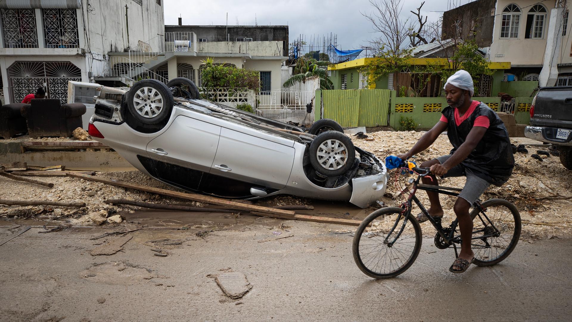 Ein Mann fährt auf einem Fahrrad an einem zerstörteten Auto in Montego Bay vorbei.