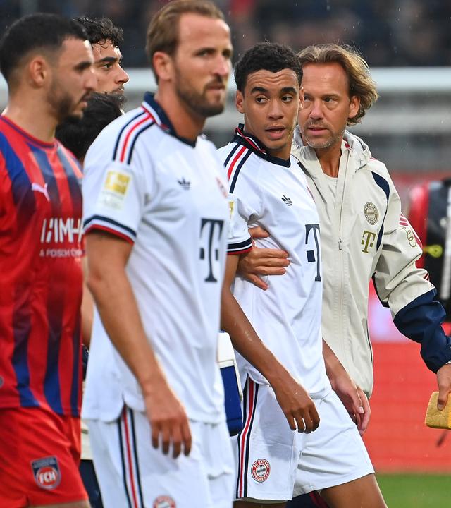 Dr. Peter Ueblacker (Mannschaftsarzt FCB) und Harry Kane (links) begleiten Jamal Musiala vom Platz