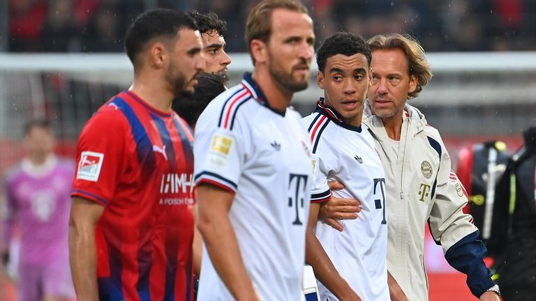 Dr. Peter Ueblacker (Mannschaftsarzt FCB) und Harry Kane (links) begleiten Jamal Musiala vom Platz