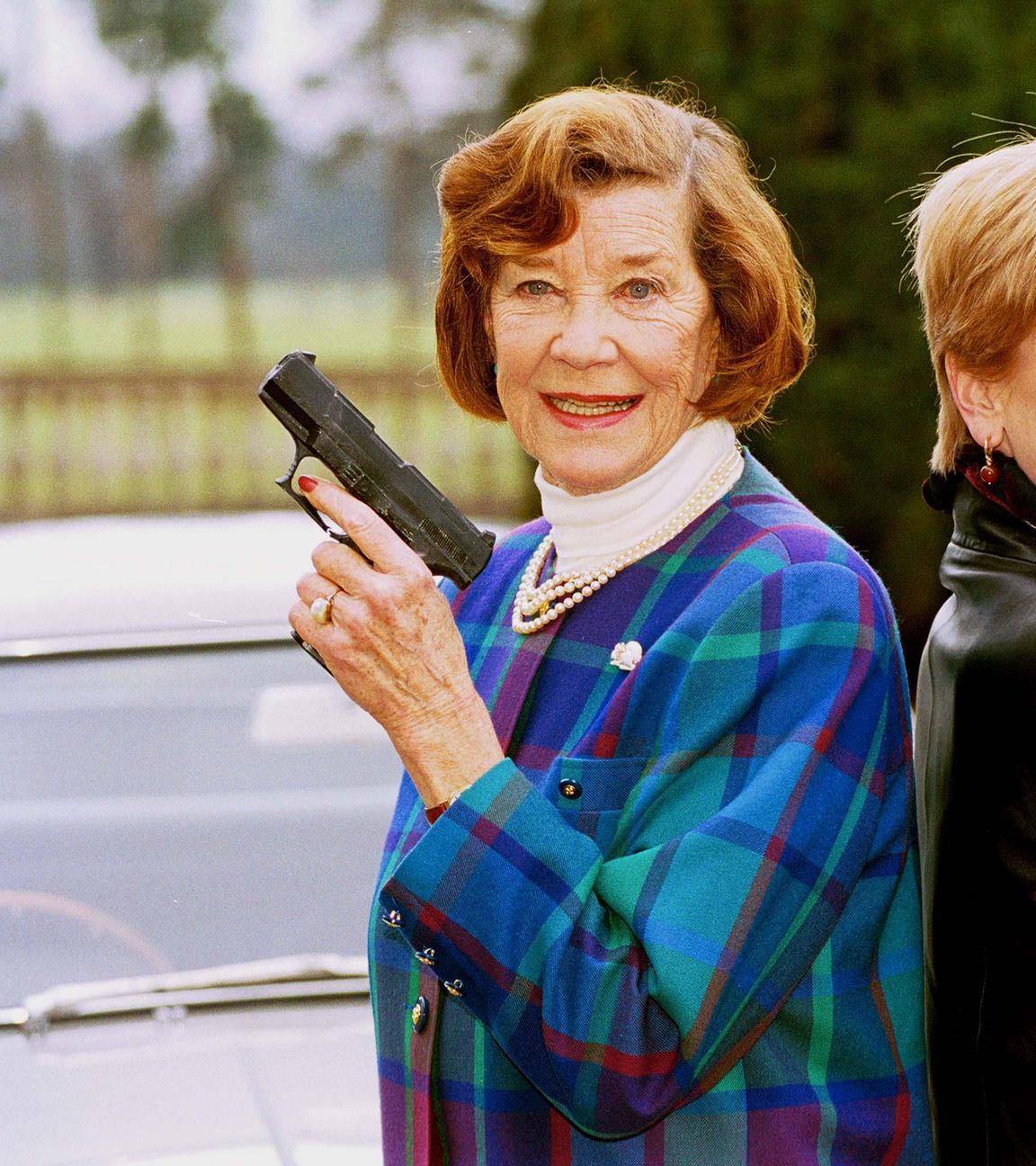 Die Schauspielerinnen Lois Maxwell (l) und Samantha Bond, die beide die Rolle der Miss Moneypenny in verschiedenen James-Bond-Filmen spielten, posieren mit Waffen aus früheren James-Bond-Filmen