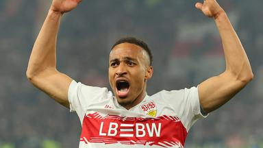 Fußballspieler Jamie Leweling im Trikot des VfB Stuttgart wirft im Spiel die Arme nach oben.