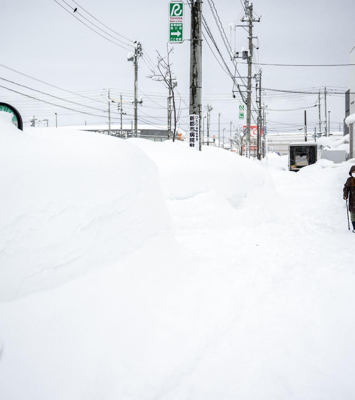 Ein Fußgänger läuft durch hohen Schnee auf einem Bürgersteig in der japanischen Stadt Aomori.