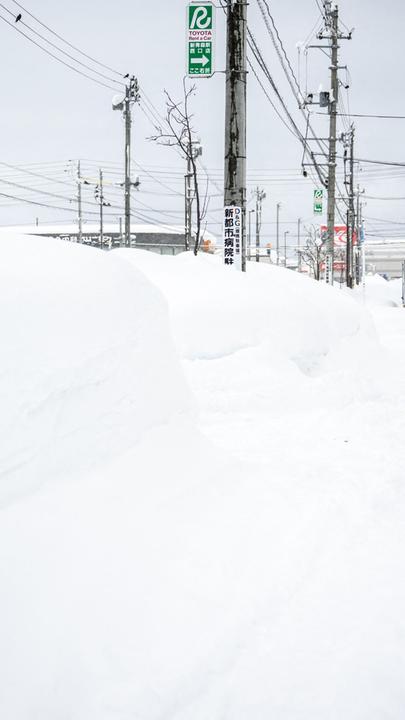 Ein Fußgänger läuft durch hohen Schnee auf einem Bürgersteig in der japanischen Stadt Aomori.