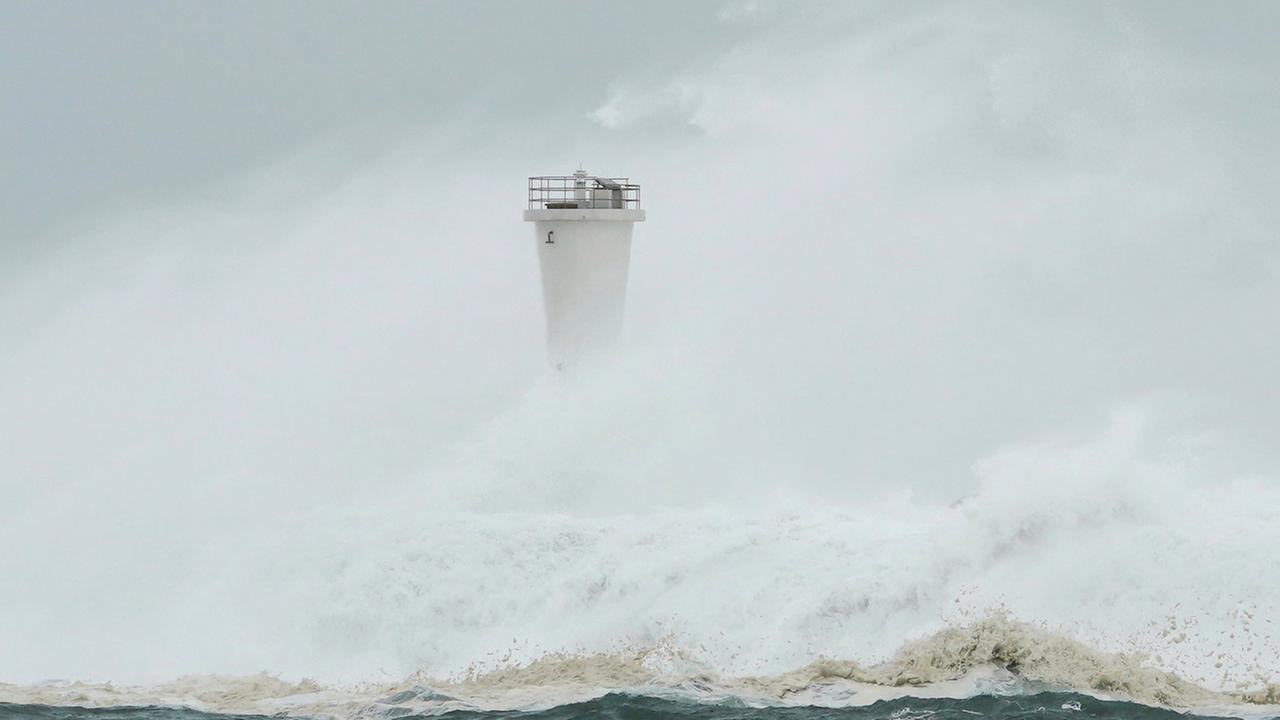 Wellen schlagen gegen die Mole und einen Leuchtturm im Hafen von Kiho