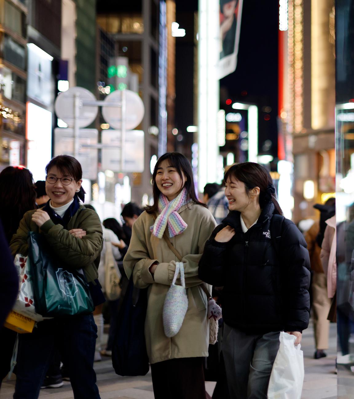 Drei Japanerinnen laufen lächelnd durch die Shoppingmeile von Tokyo mit Tüten in der Hand.