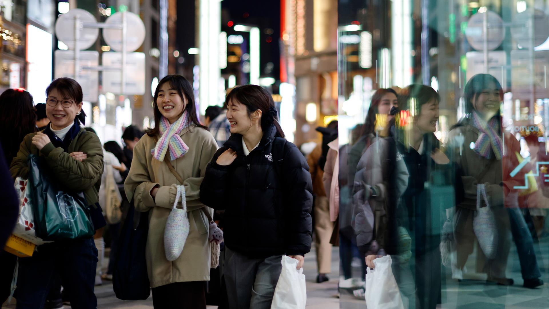 Drei Japanerinnen laufen lächelnd durch die Shoppingmeile von Tokyo mit Tüten in der Hand.