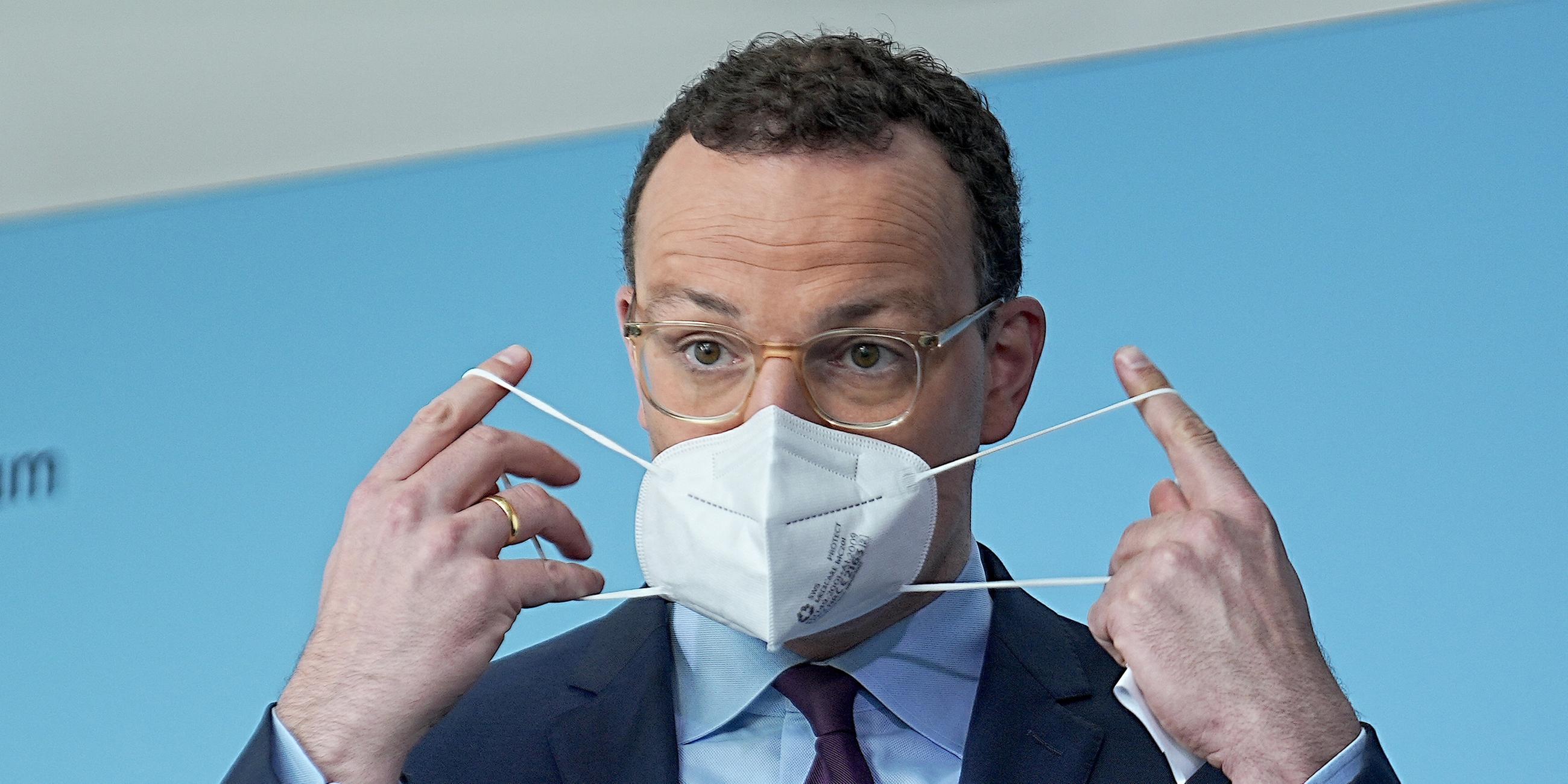 Jens Spahn legt eine Coronamaske an (Archiv)