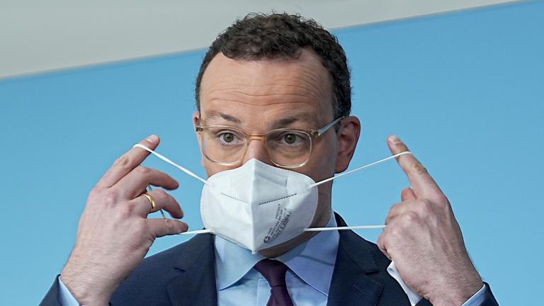 Jens Spahn legt eine Coronamaske an (Archiv)