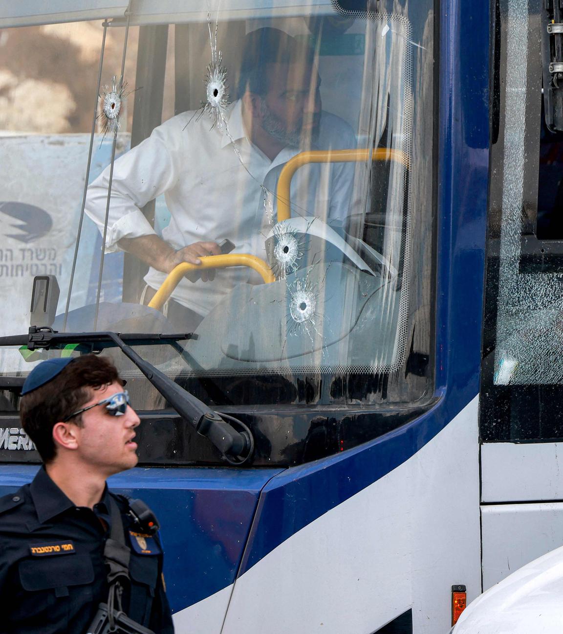Zwei israelische Polizisten gehen am 08.09.2025 an der Windschutzscheibe eines Busses vorbei, die mit Einschusslöchern übersät ist, am Ort einer Schießerei an der Kreuzung Ramot in dem von Israel annektierten Ostjerusalem. 