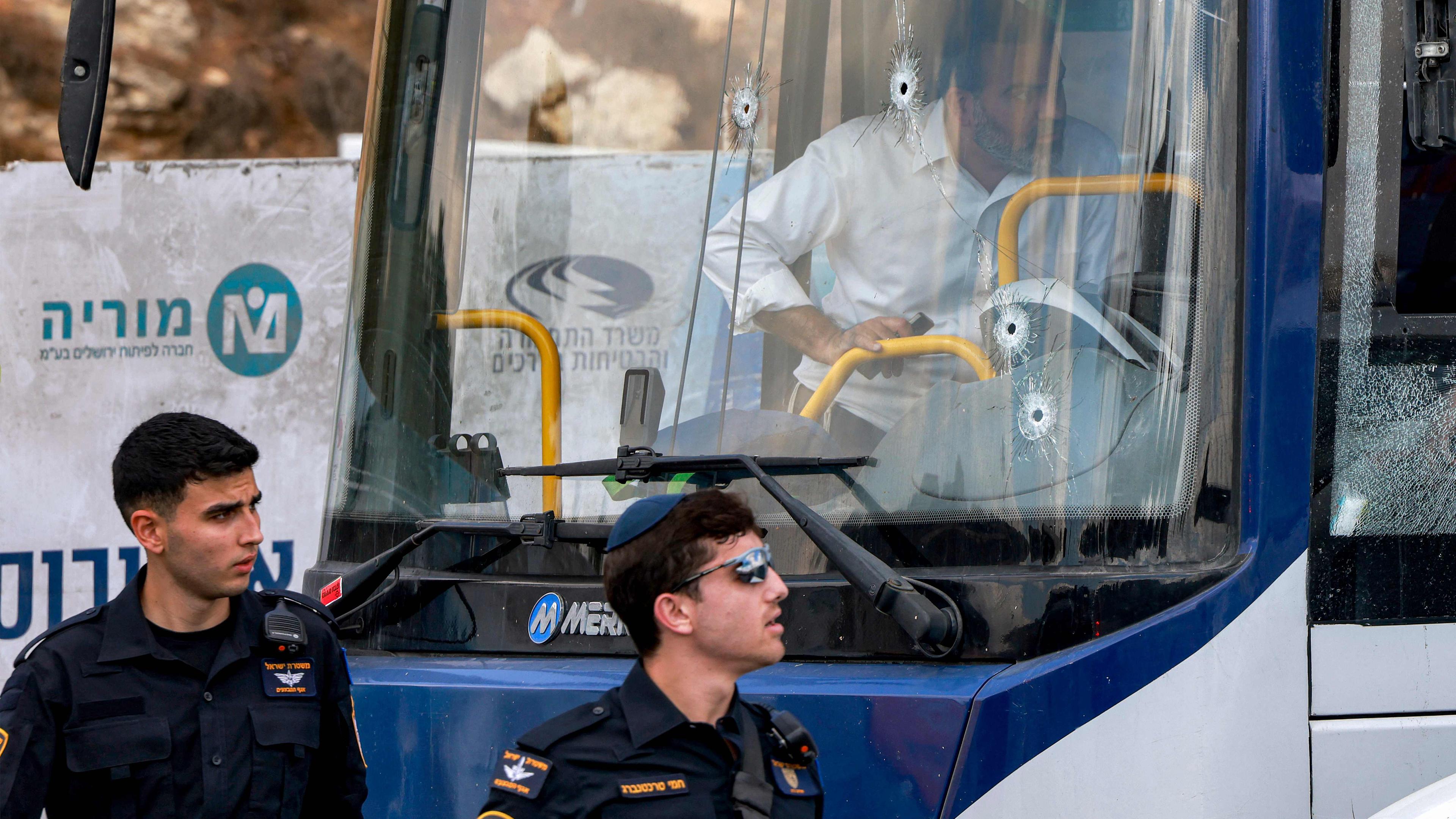 Zwei israelische Polizisten gehen am 08.09.2025 an der Windschutzscheibe eines Busses vorbei, die mit Einschusslöchern übersät ist, am Ort einer Schießerei an der Kreuzung Ramot in dem von Israel annektierten Ostjerusalem. 