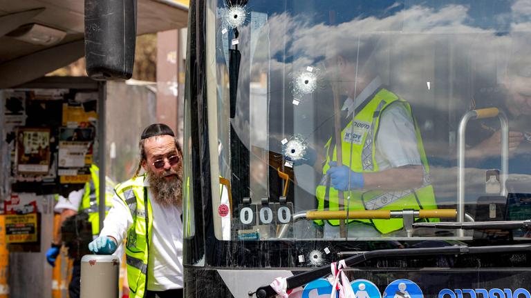 Der beschädigte Bus mit Einschusslöchern in der Windschutzscheibe. Neben dem Bus stehen Menschen mit Warnwesten.