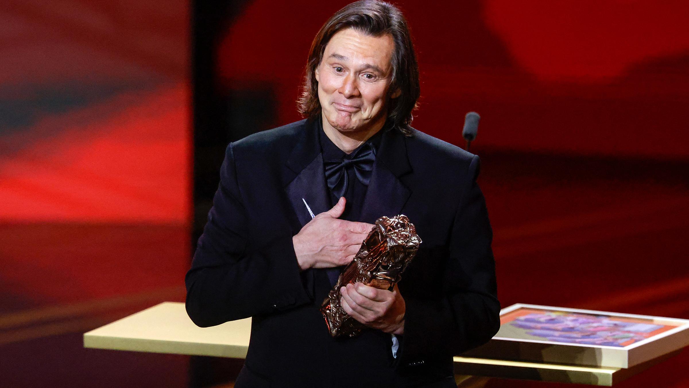 Schauspieler Jim Carrey posiert sichtlich gerührt mit einem Preis in der Hand.