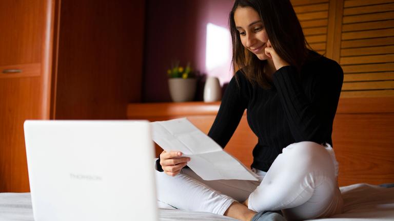 Junge Frau sitzt vor ihrem Laptop und füllt den Lebenslauf für ihr Profil auf einem Karriere-Portal aus.