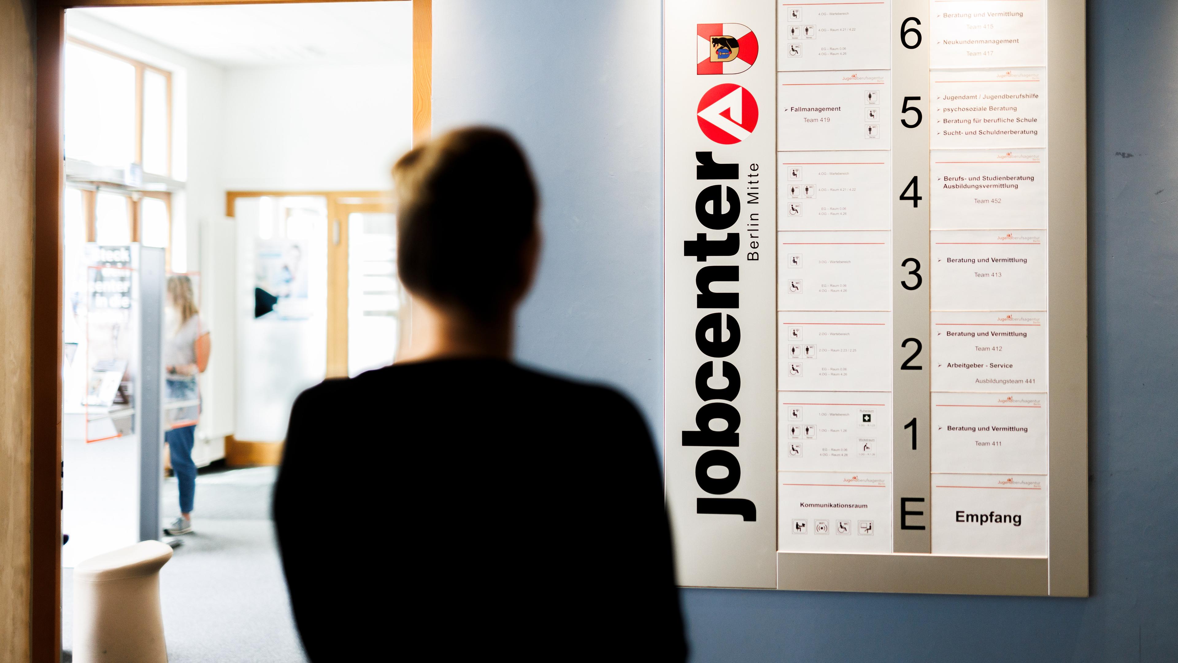 Eine Frau steht in vor einer Informationstafel im Eingangsbereich eines Jobcenter