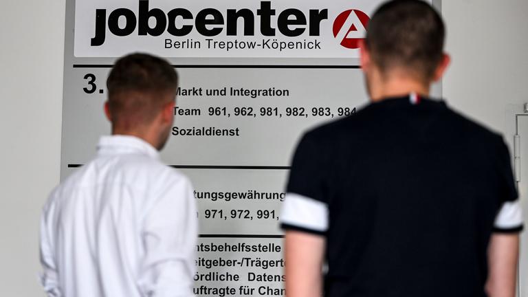 Zwei Männer stehen vor einer Informationstafel im Jobcenter Berlin Treptow-Köpenick.