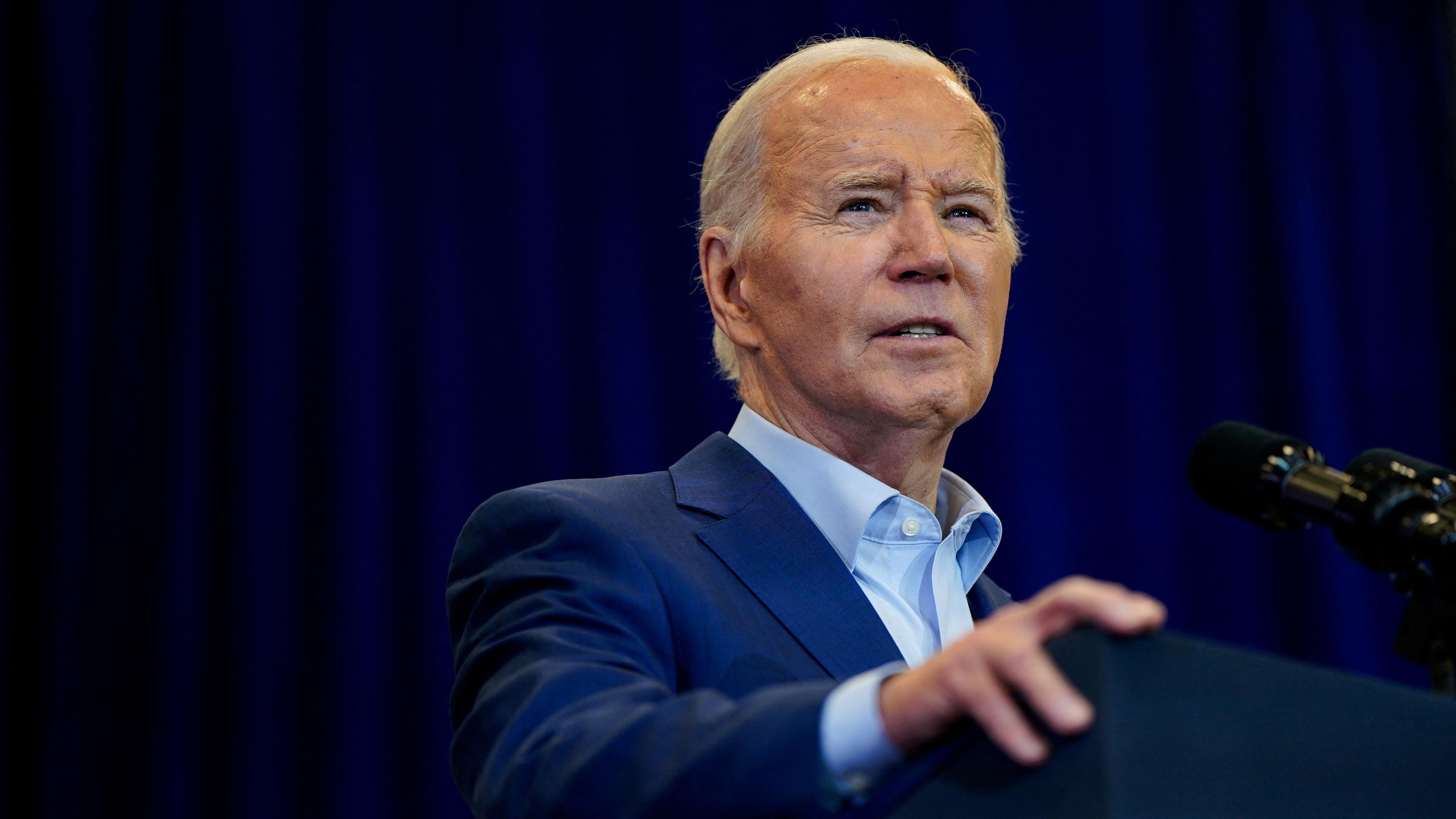 Joe Biden steht an einem Rednerpult im Hintergrund ist ein blauer Vorhang. 