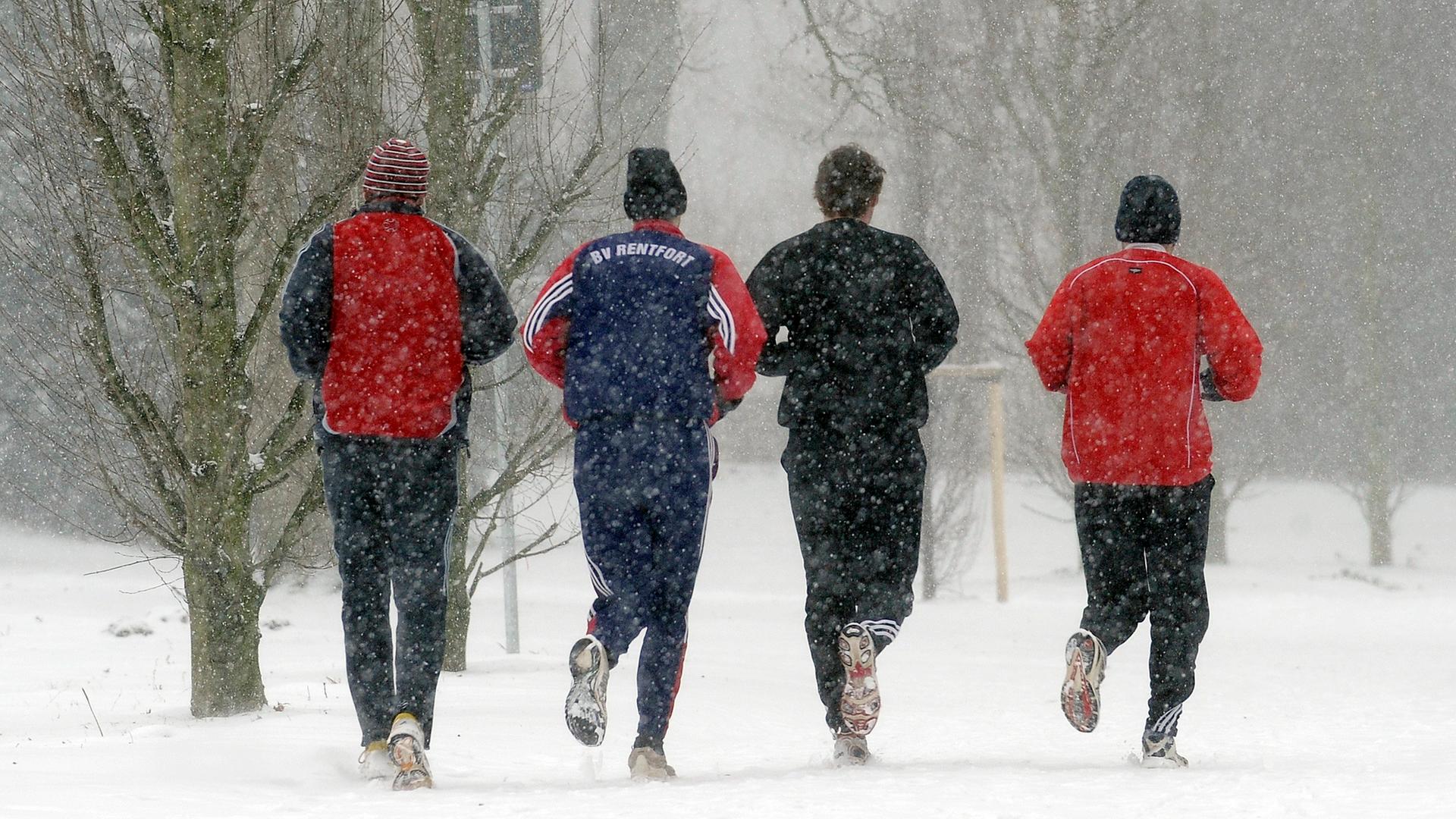 Vier Männer joggen nebeneinander über einen verschneiten Weg.